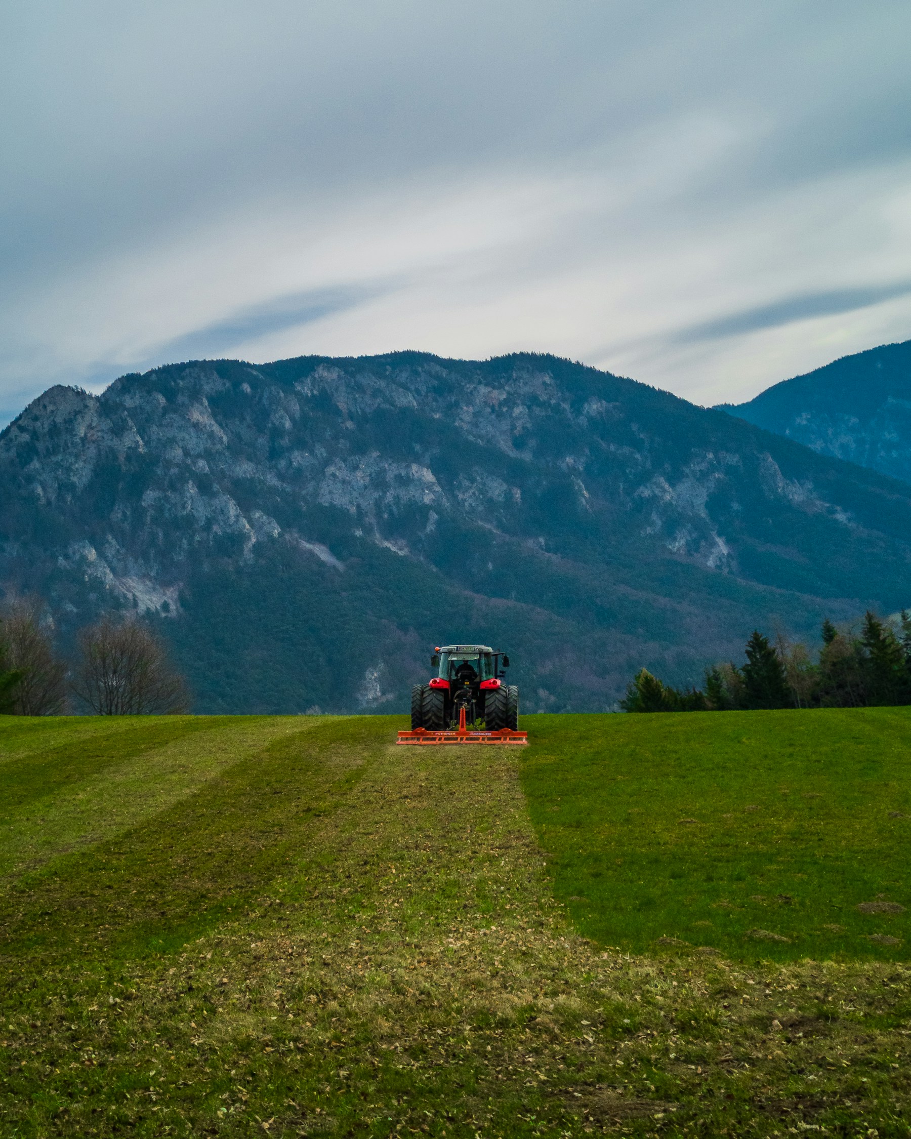 Grüne Nutzfläche mit Traktor vor einer österreichischen Berglandschaft